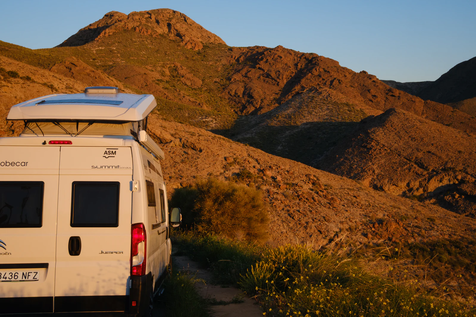 Furgoneta camper con techo elevado en un camino de tierra de montaña al atardecer